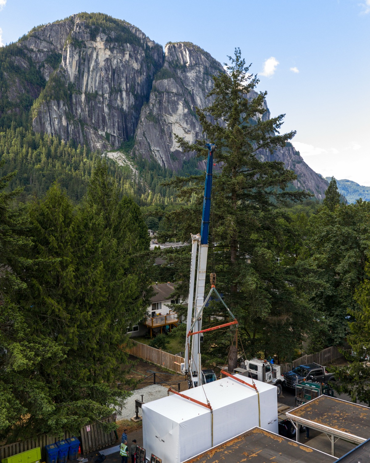 Crane lifting a wrapped ADU module with a granite bluff behind