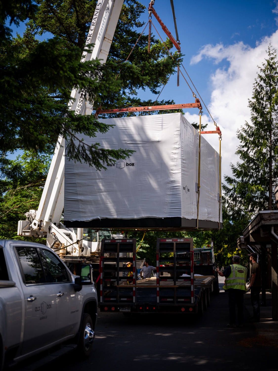 Wrapped ADU module lifting off a trailer, crew standing below