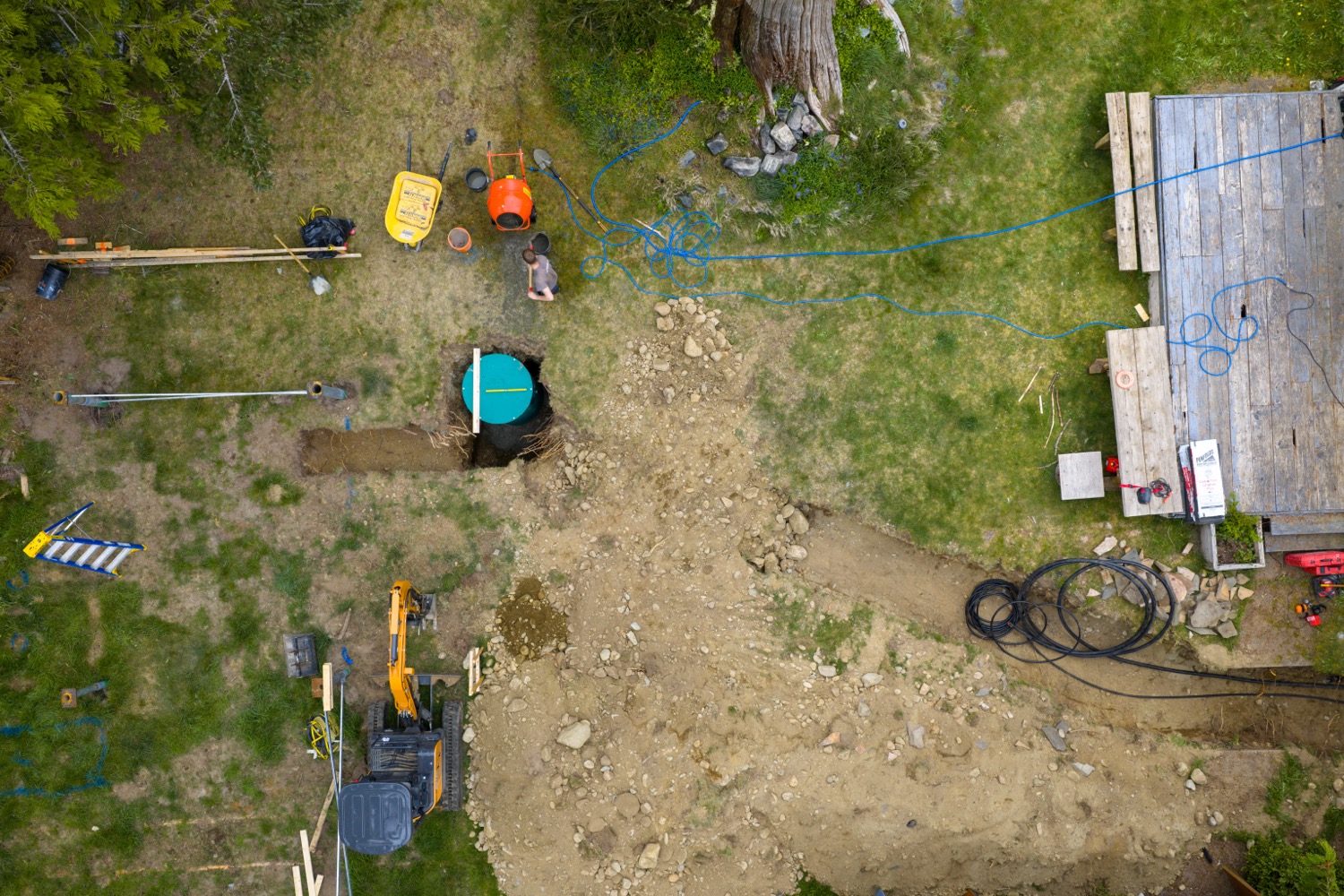 Aerial of a backyard excavation with a tank in the hole and a mini excavator
